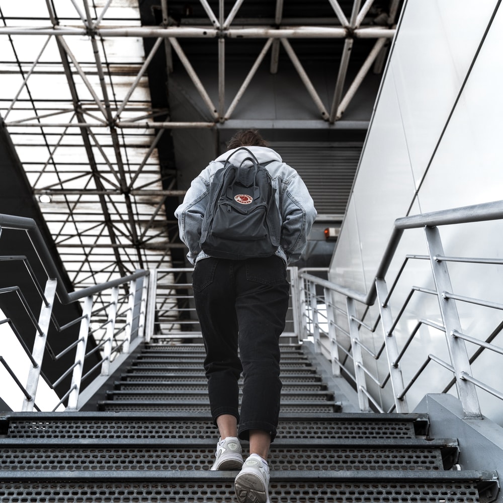 Man In Blue Jacket And Black Pants Walking On Black Staircase raster image