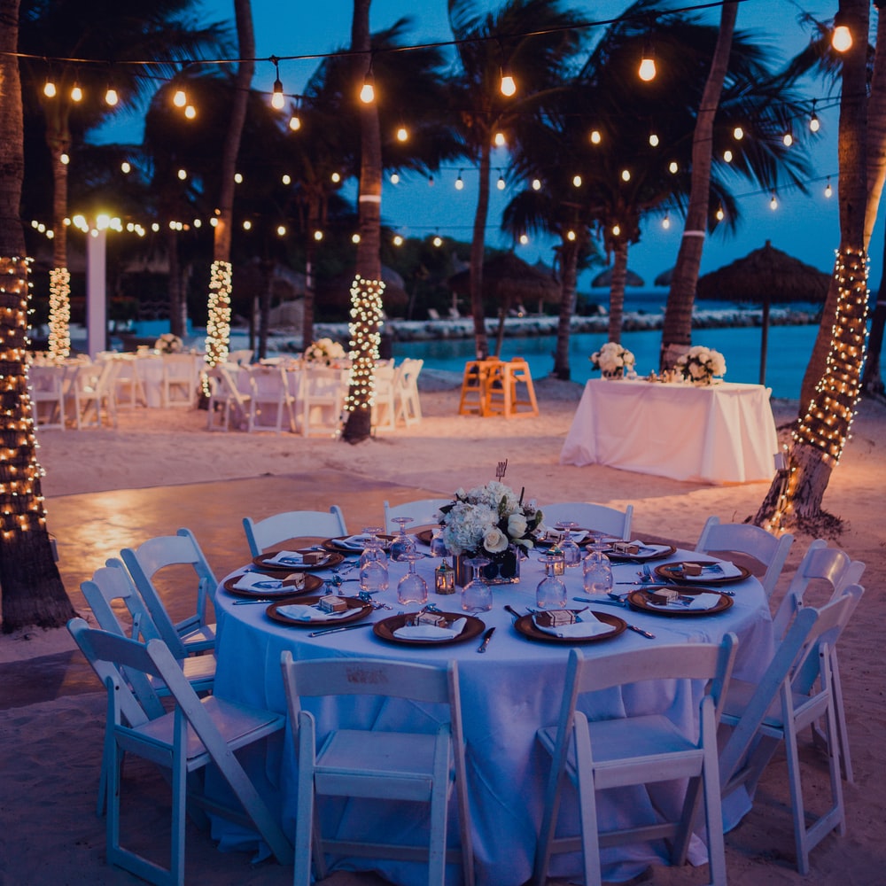 White Table With Chairs And Lighted String Lights During Night Time