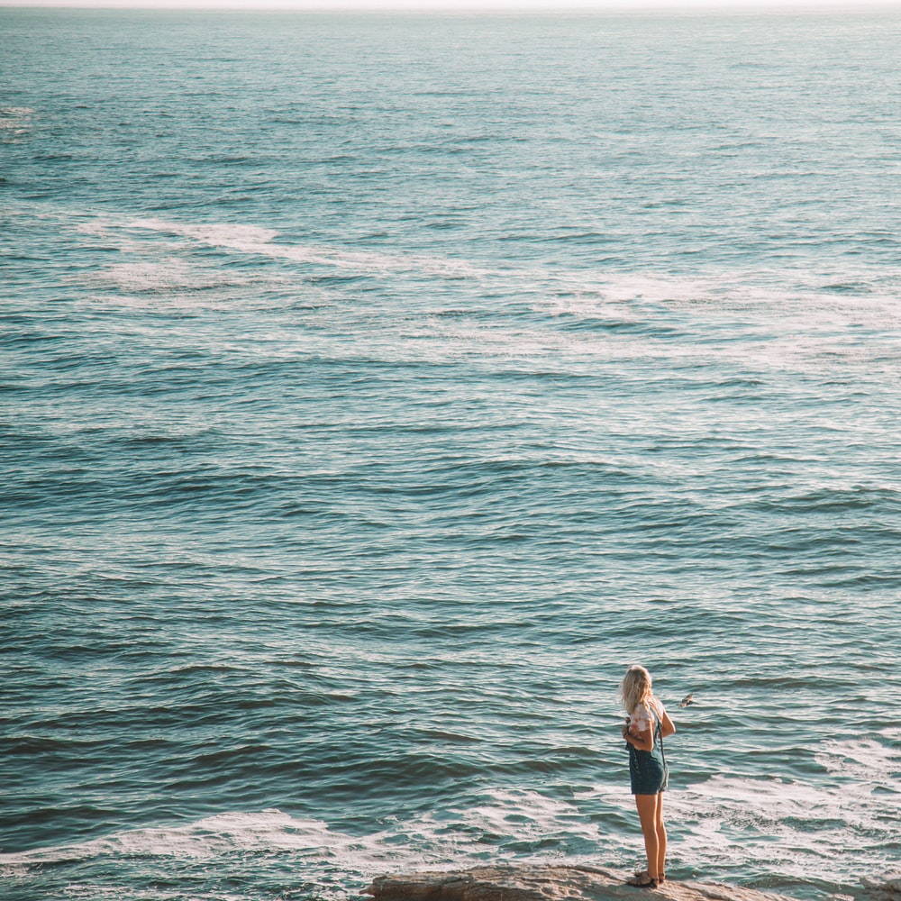 Woman In White Shirt And Black Shorts Standing On Sea Shore During Daytime raster image