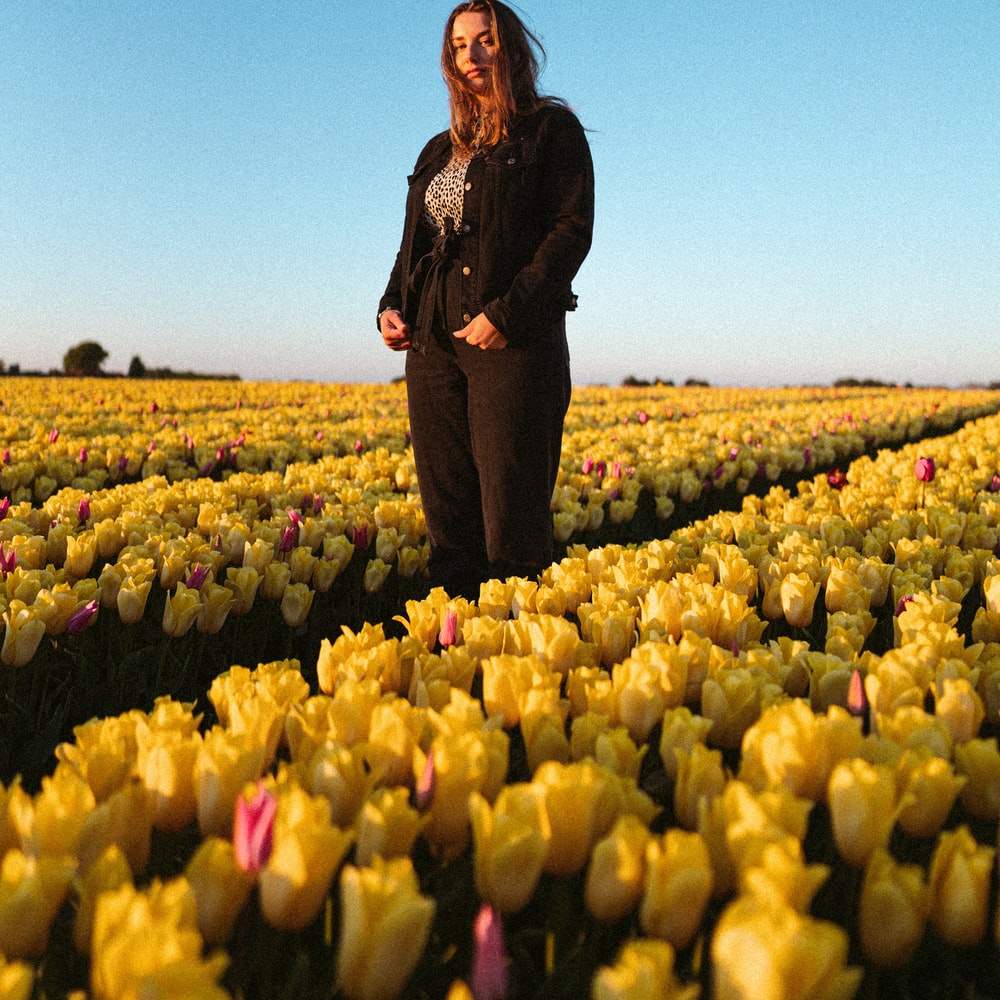 Woman In Black Jacket Standing On Yellow Flower Field During Daytime