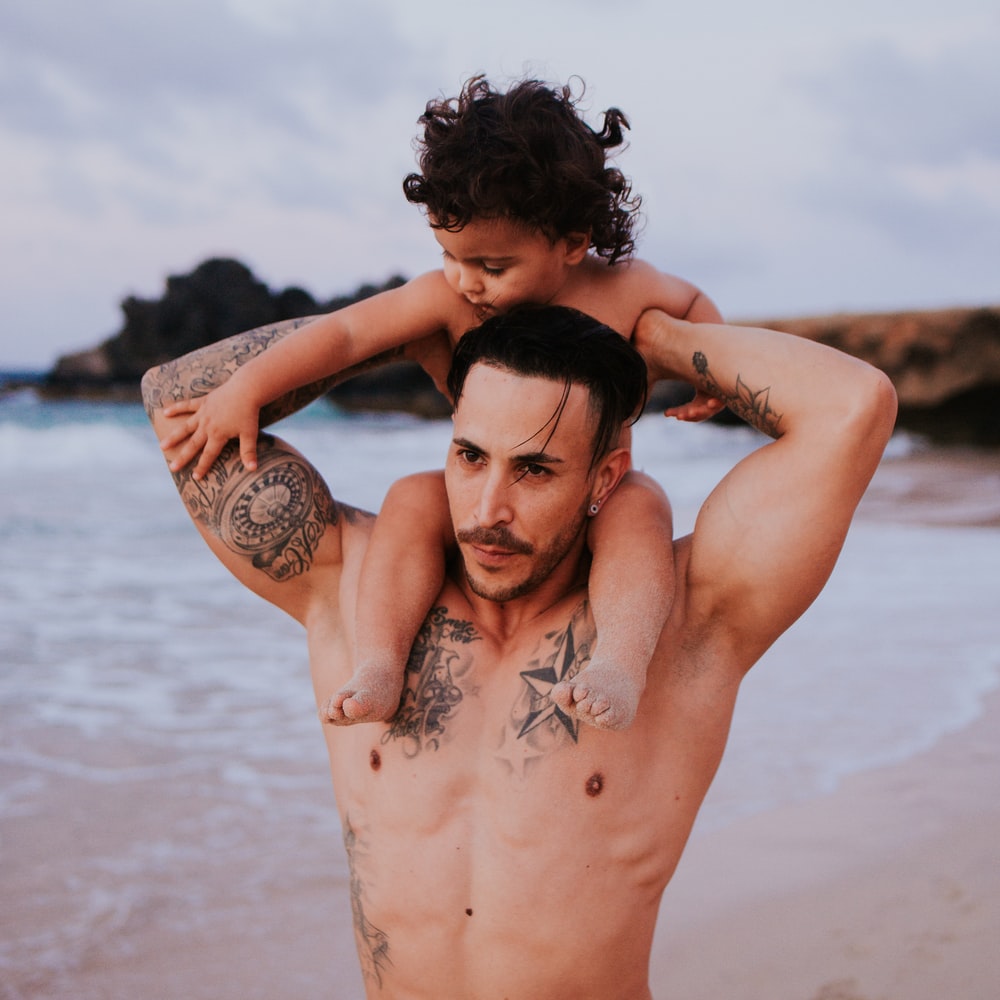 Topless Woman With Black Tattoo On Her Back Standing On Beach During Daytime raster image