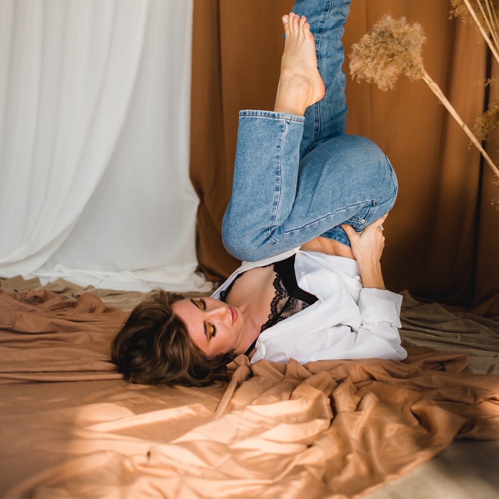 Woman In White Shirt And Blue Denim Jeans Lying On Bed