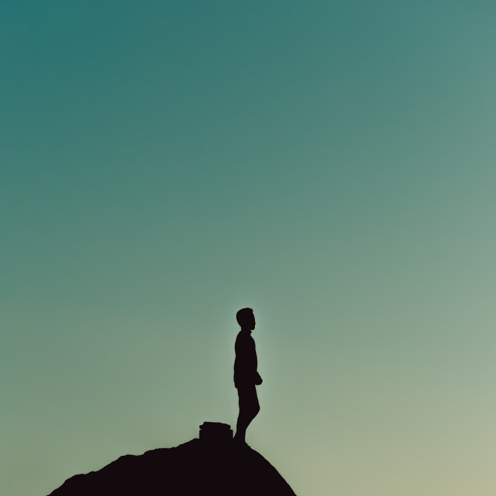 Silhouette Of Man Standing On Rock Formation During Daytime