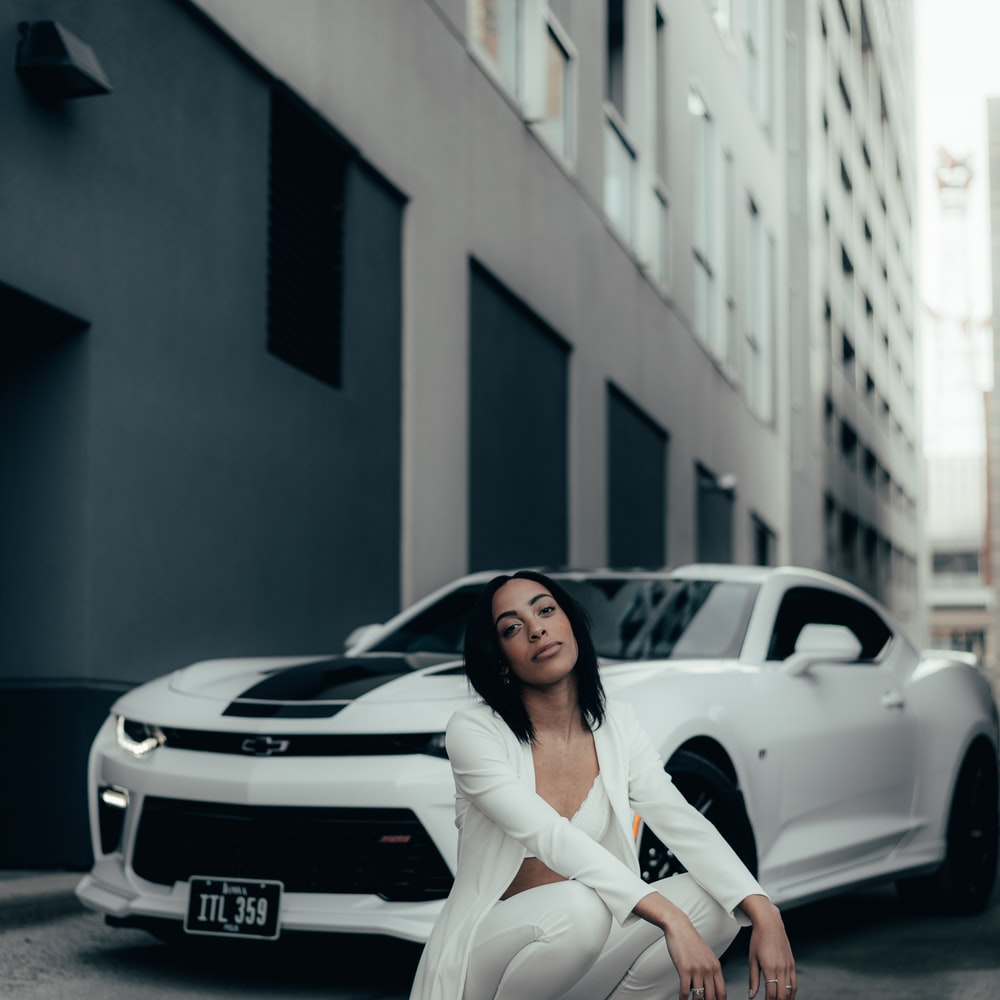 Woman In White Long Sleeve Shirt And White Pants Sitting On White Car raster image