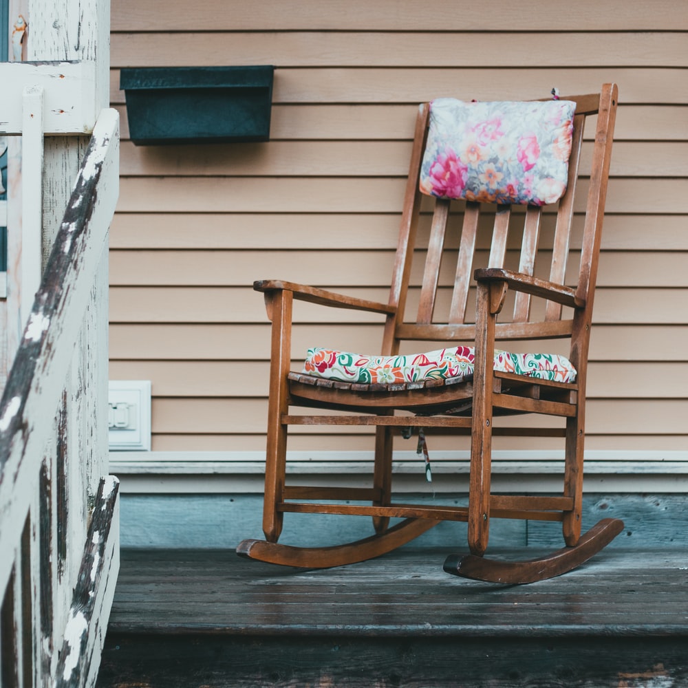 Brown Wooden Rocking Chair Near White Wooden Fence