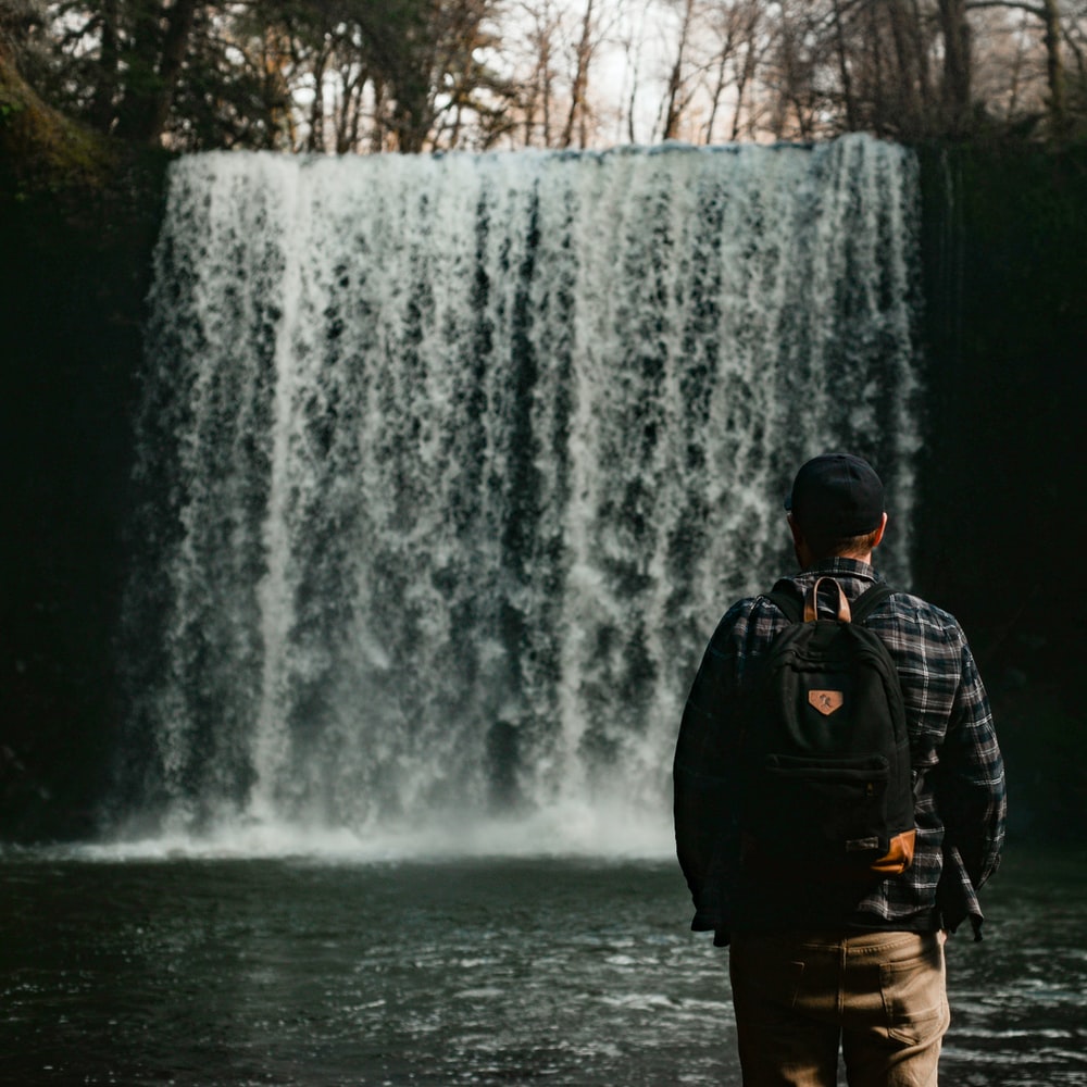 Man In Black Jacket Standing In Front Of Waterfalls raster image