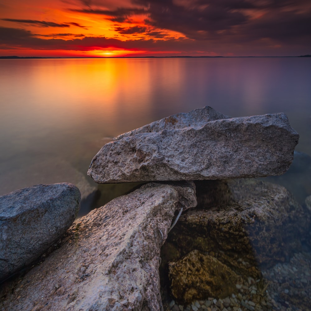 Gray And Black Rocks Near Body Of Water During Sunset