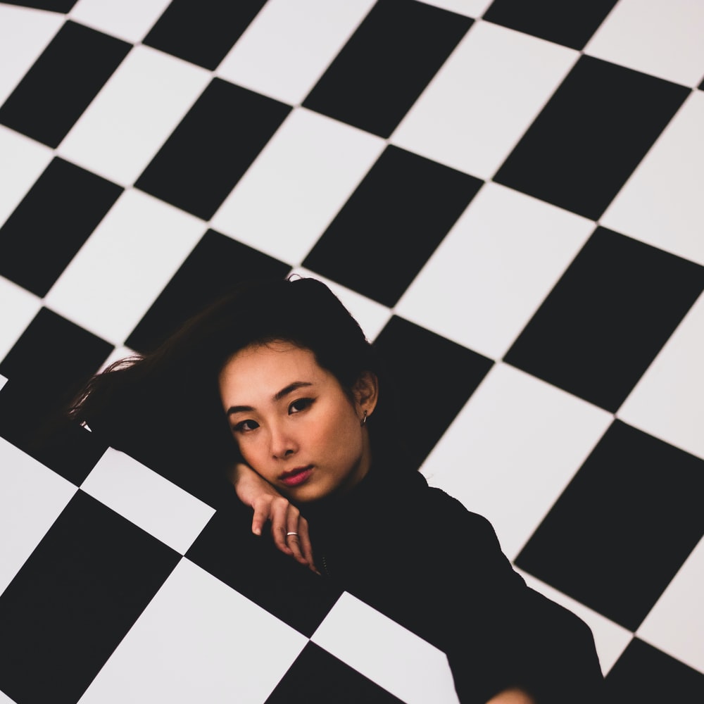 Girl In Black Long Sleeve Shirt Lying On Black And White Checkered Floor raster image