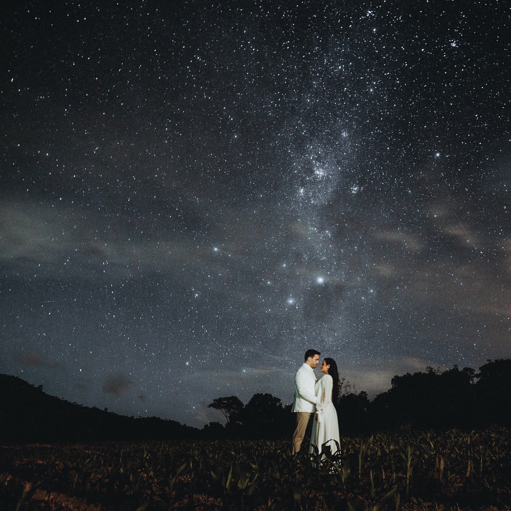 Man And Woman Standing On Brown Grass Field Under Starry Night