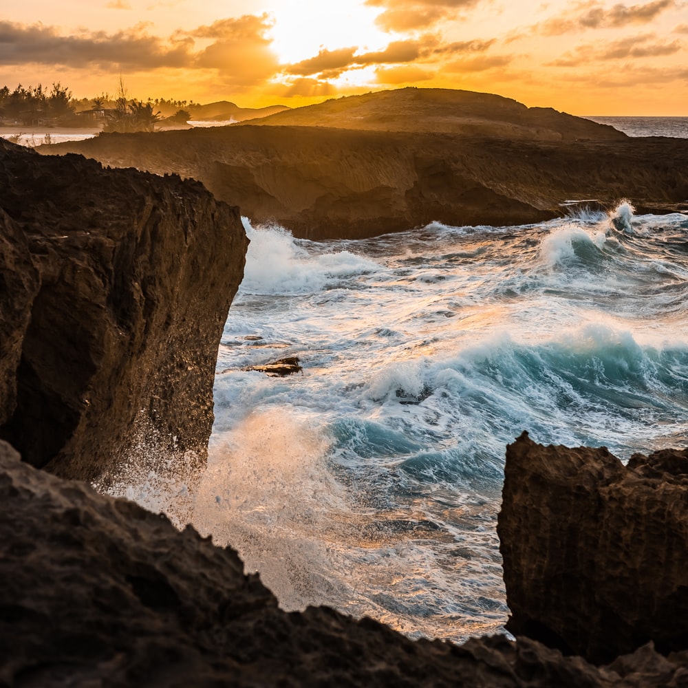 Ocean Waves Crashing On Brown Rocky Shore During Sunset raster image