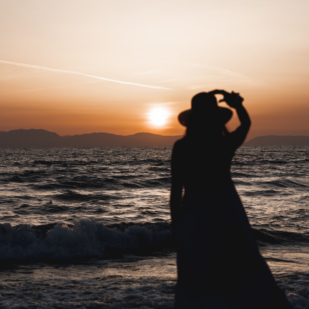 Silhouette Of Woman Standing On Seashore During Sunset raster image
