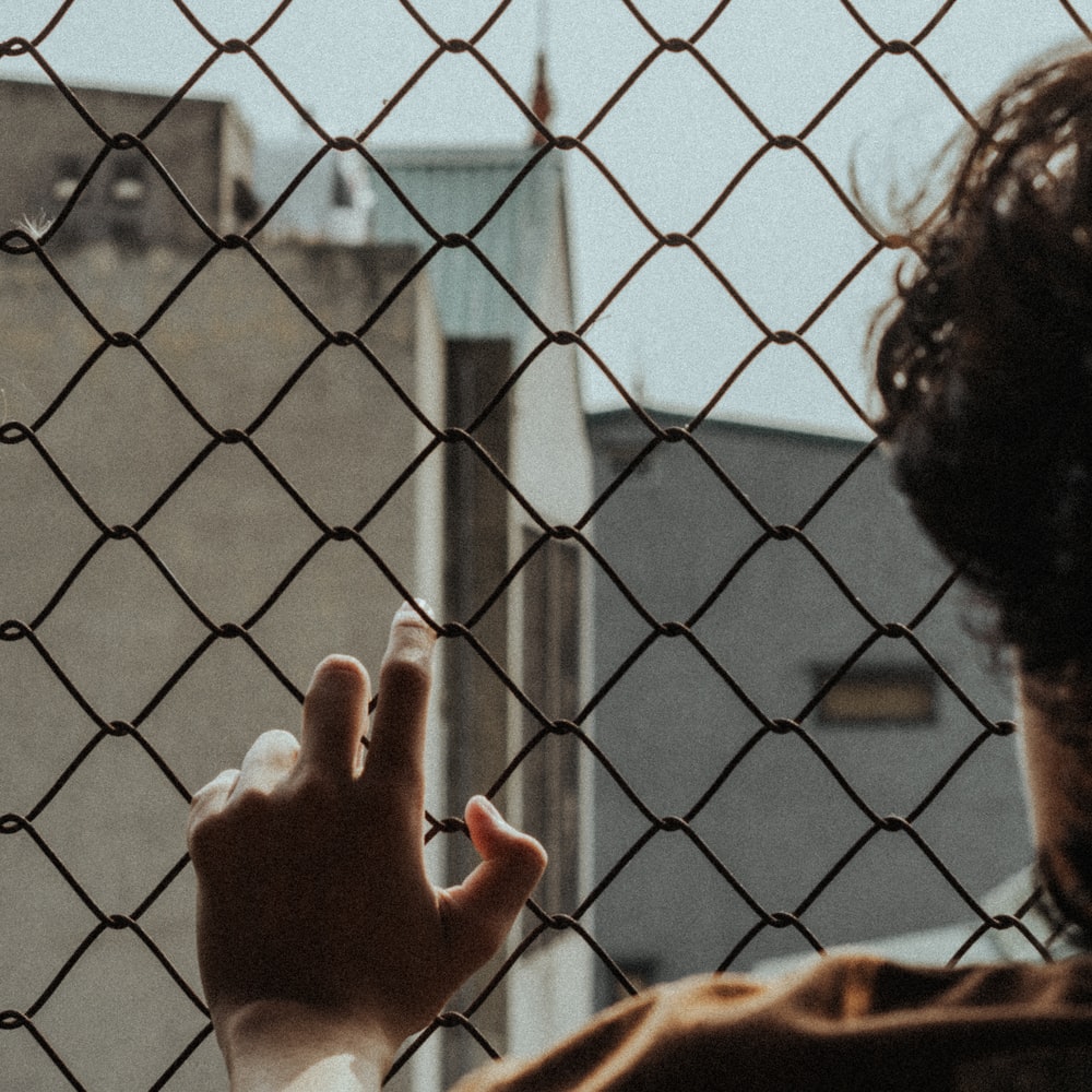 Person In White Long Sleeve Shirt Holding On Gray Metal Fence raster image